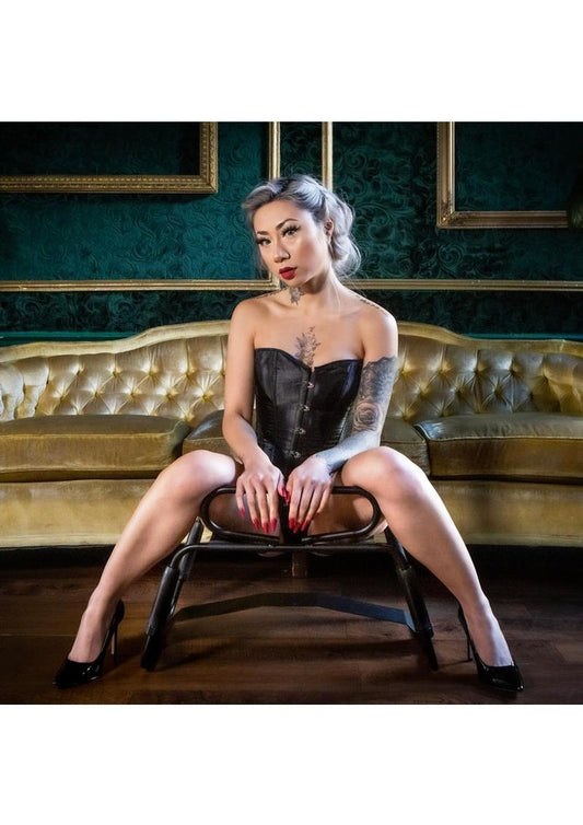 Woman in a black corset sitting on a chair in a room with green walls and gold accents.